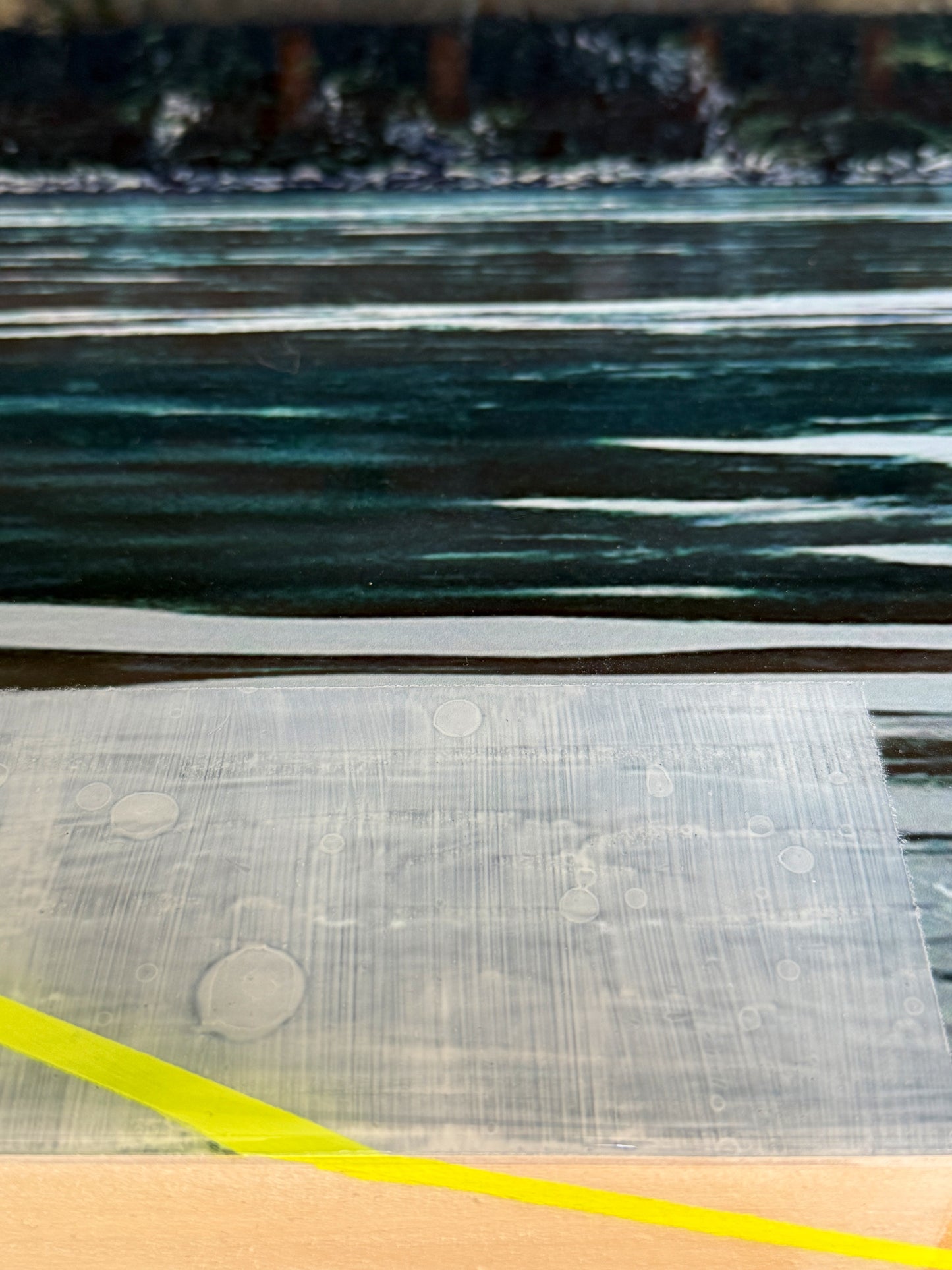 Detail view of Christen Oatley's 'Alaskan Mist' mixed media artwork, showcasing layered resin texture, a vibrant yellow accent line, and reflective ocean-inspired brushwork. Highlights the dimensional finish and handcrafted surface of the original coastal art piece.