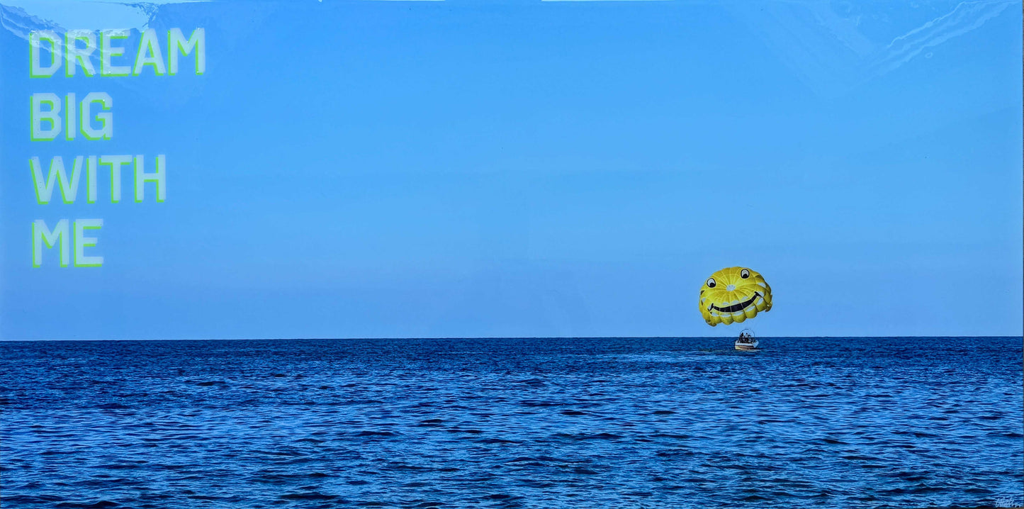Dream Big With Me' original landscape mixed media artwork by Christen Oatley, featuring a bright yellow smiley face parasail floating over the deep blue Mediterranean Sea beneath lime green acrylic text on a 24x48 inch Canadian birchwood panel.