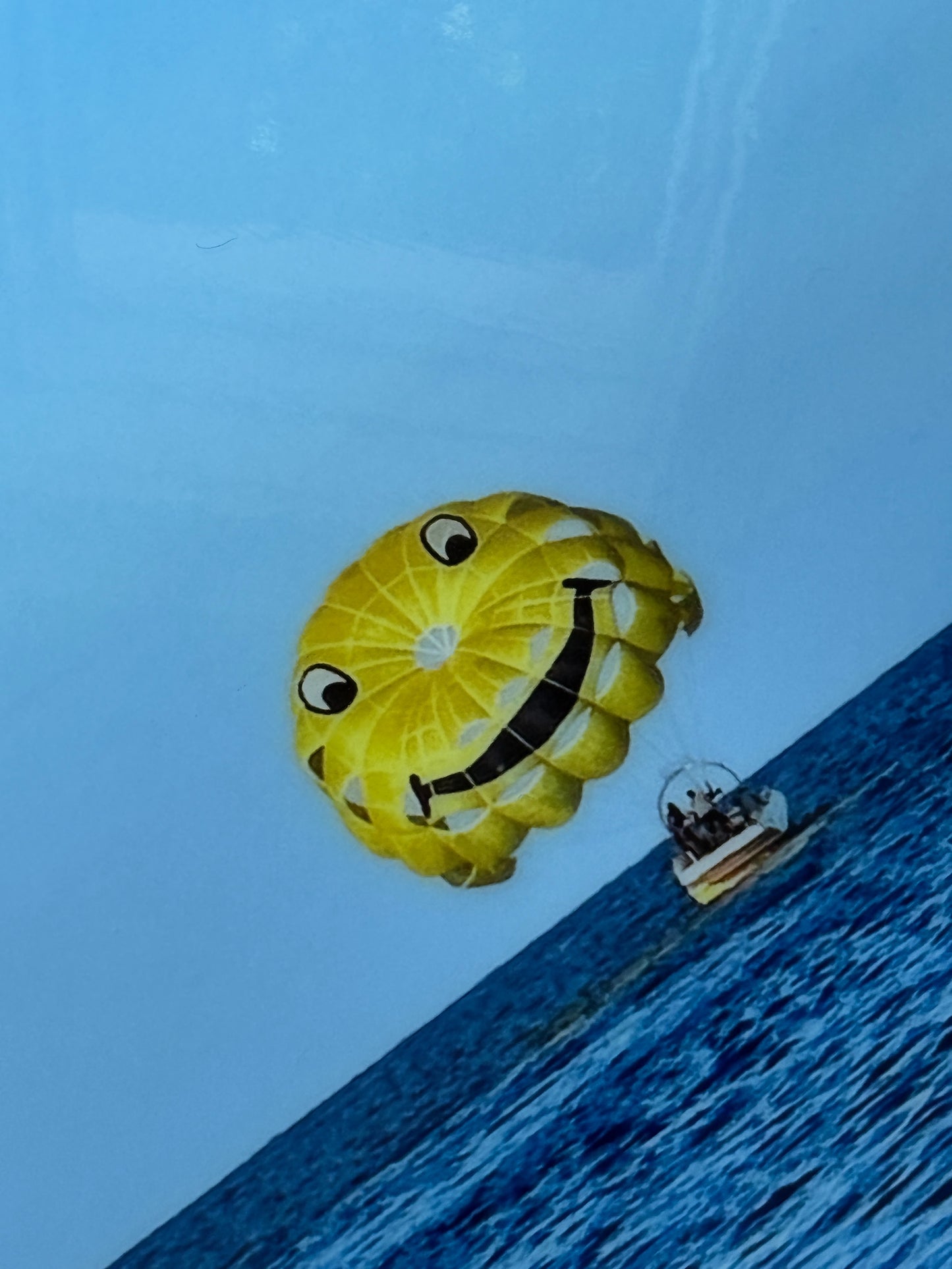 Close up: Dream Big With Me' original landscape mixed media artwork by Christen Oatley, featuring a bright yellow smiley face parasail floating over the deep blue Mediterranean Sea beneath lime green acrylic text on a 24x48 inch Canadian birchwood panel.