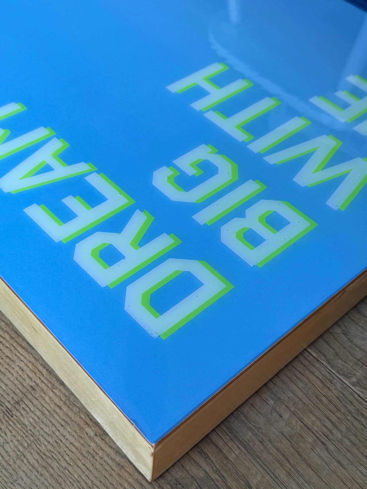 Close up: Dream Big With Me' original landscape mixed media artwork by Christen Oatley, featuring a bright yellow smiley face parasail floating over the deep blue Mediterranean Sea beneath lime green acrylic text on a 24x48 inch Canadian birchwood panel.