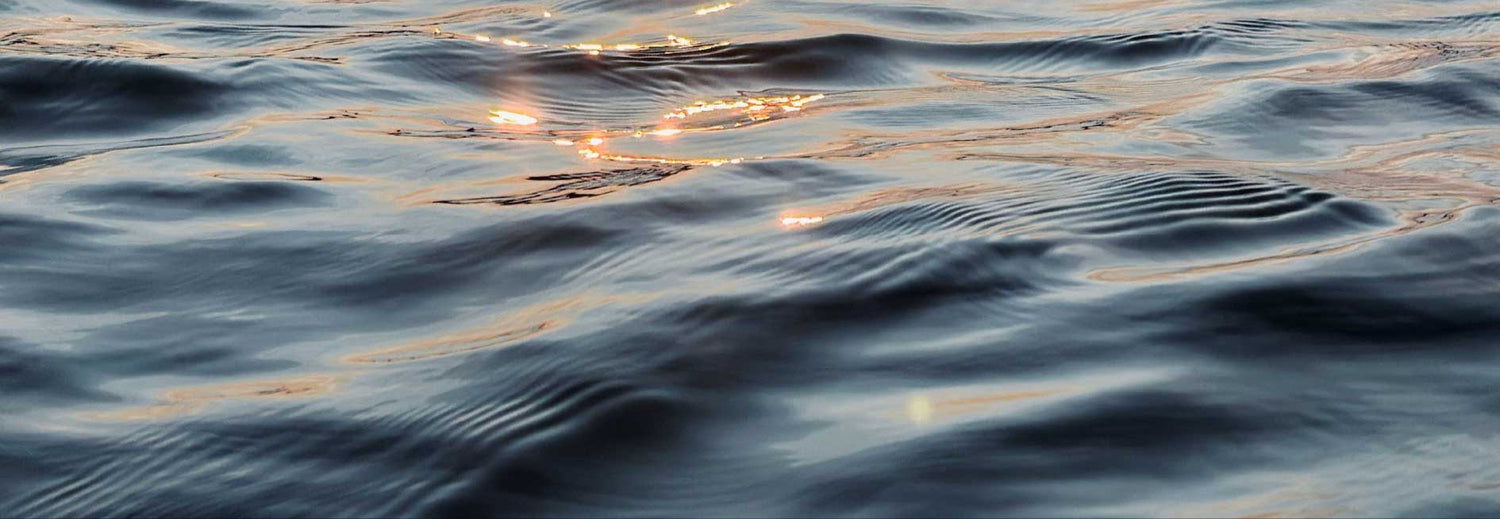 Close-up of calm ocean waves with soft ripples reflecting golden sunlight, creating a peaceful and serene atmosphere.