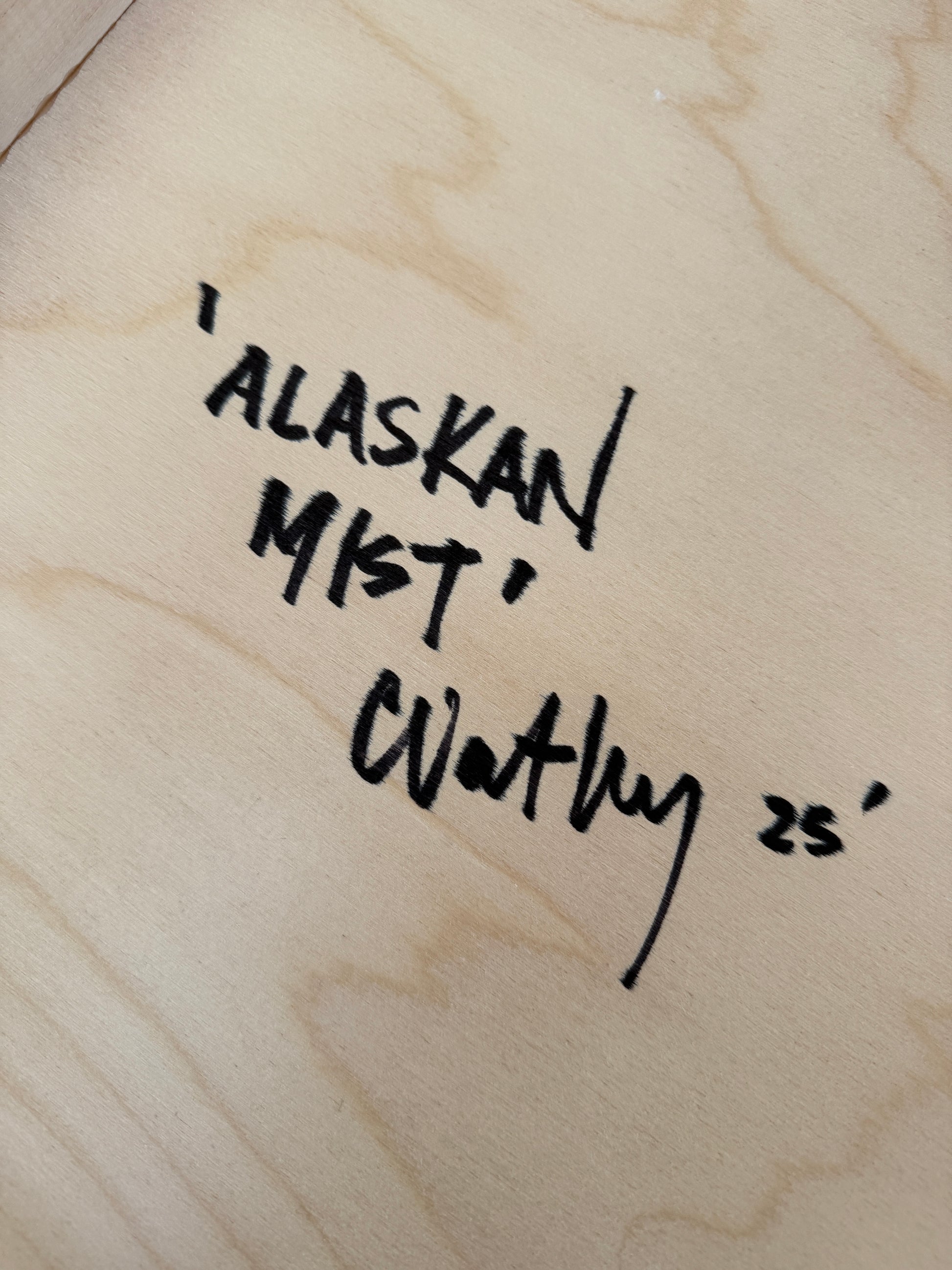 Artist signature on the back of 'Alaskan Mist' by Christen Oatley, handwritten in black ink on natural birchwood panel, including the artwork title and year '25.